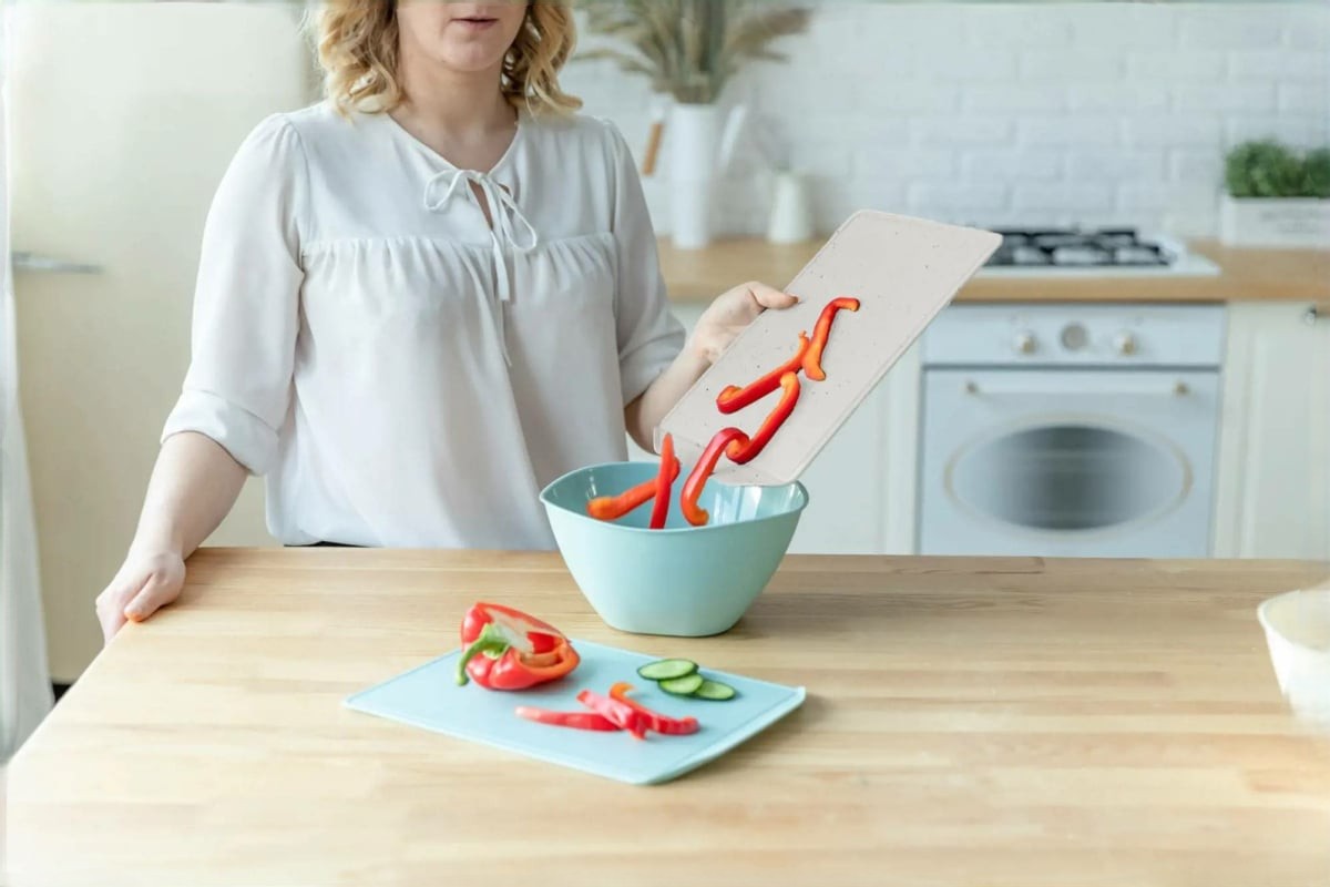 Een vrouw gebruikt een snijplank om groenten te snijden.