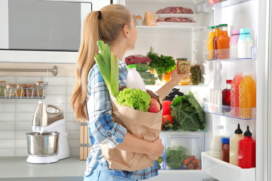 Het meisje legt de boodschappen in de koelkast.